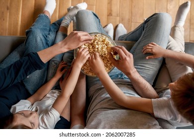 Close up crop top down of parents with little children relax at home eat snacks watching TV. Young family with small kids rest on sofa with popcorn have movie fil television time together.