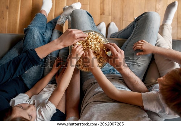 Close up\
crop top down of parents with little children relax at home eat\
snacks watching TV. Young family with small kids rest on sofa with\
popcorn have movie fil television time\
together.