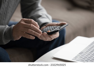 Close up crop view hands of unknown senior man count using calculator calculates expenses and incomes, manage household budget, pay taxes online in modern bank application, makes financial analysis