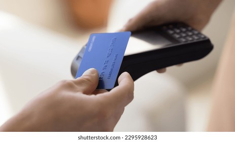 Close up crop view unknown male makes easy, convenient e-payment, holds plastic card against contactless payment terminal equipment, paying for services, food or shopping use wireless NFC technology