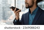 Close up cropped of African American businessman executive in suit recording audio voice message on smartphone, holding phone near mouth, dictating, chatting online by speakerphone in social network