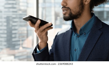 Close up cropped of African American businessman executive in suit recording audio voice message on smartphone, holding phone near mouth, dictating, chatting online by speakerphone in social network - Powered by Shutterstock