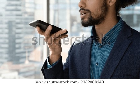 Close up cropped of African American businessman executive in suit recording audio voice message on smartphone, holding phone near mouth, dictating, chatting online by speakerphone in social network