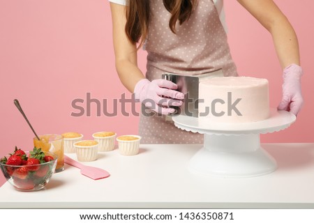 Close up cropped chef cook confectioner or baker in white t-shirt cooking at table isolated on pink pastel background in studio. Cream application cake making process. Mock up copy space food concept