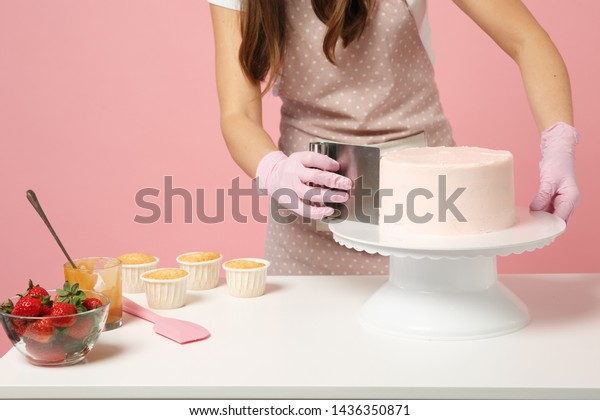 Close up cropped chef cook confectioner or baker\
in white t-shirt cooking at table isolated on pink pastel\
background in studio. Cream application cake making process. Mock\
up copy space food\
concept