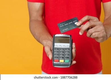 Close Up Cropped Delivery Employee Man 20s In Red T-shirt Uniform Work Courier Service Hold Wireless Bank Payment Terminal To Process Acquire Credit Card Payments Isolated On Yellow Background Studio