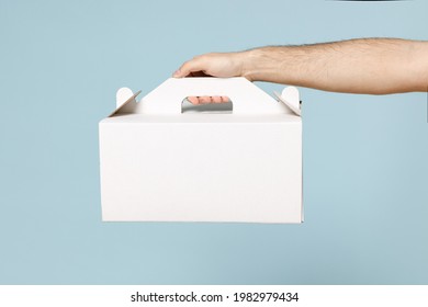 Close up cropped employee courier man hold in hand cake dessert unmarked clear empty blank cardboard box isolated on blue color background mock up Delivery service concept Copy space Advertising area