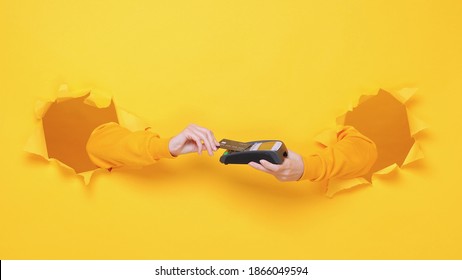 Close up cropped female hand hold wireless bank terminal to process acquire credit card payments pay isolated through torn yellow background studio Copy space place for text or image workspace mock up - Shutterstock ID 1866049594