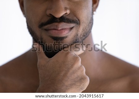 Close up cropped front face view handsome sensual 35s African ethnicity guy with naked shoulders, hand touches bearded chin. Self-groom, skin care products, advertisement of cosmetics for men concept