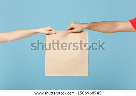 Close up cropped hands hold brown clear empty blank craft paper bag food for takeaway isolated on blue background. Packaging template mock up. Delivery service concept. Copy space. Advertising area