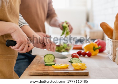 Close up cropped image of cutting board and couple cutting vegetables in the kitchen together, preparing food meal at home. Vegetarian healthy food 商業照片 © 