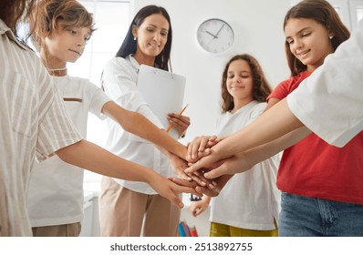 Close up cropped image of friendly female teacher and smiling teenage students in casual wear stacking their hands together, showing unity and teamwork. Back to school, education and teamwork concept. - Powered by Shutterstock