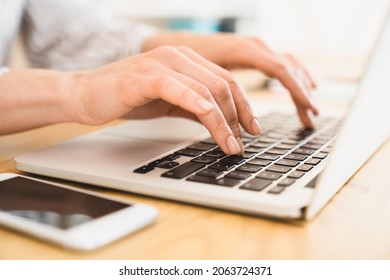 Close up cropped image of a keyboard while woman freelancer businessperson using typing on laptop, working remotely, e-learning, e-banking online, surfing Internet.