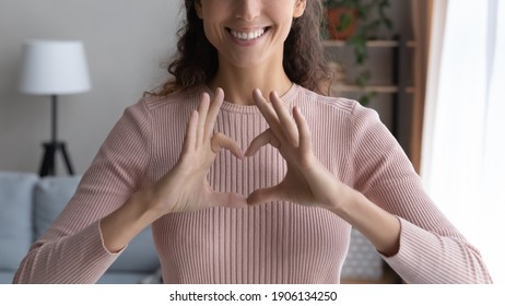 Close up cropped image smiling young woman showing heart love sign with fingers, feeling grateful indoors. Sincere happy millennial female volunteer expressing support and kindness, charity concept. - Shutterstock ID 1906134250