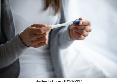 Close up cropped image woman holding plastic pregnancy test kit in hands, sitting on bed at home, young female checking results, fertility maternity concept, gynecological healthcare