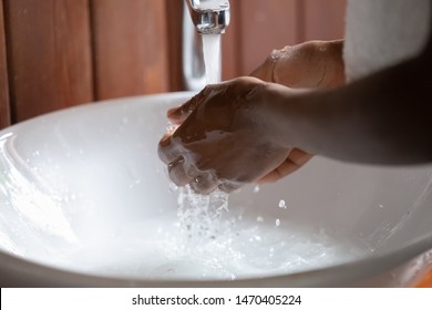 Close up cropped image young african ethnicity guy washing hands under running water in modern sink. Black guy gathering water in hands to wash face. Morning personal hygiene routine, water overuse.