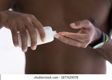 Close up cropped image young shirtless african american man pouring nourishing lotion from bottle in hand, preventing dry skin or moisturizing body, enjoying skincare routine, grooming himself.