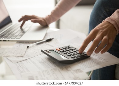 Close up cropped image young woman calculating monthly expenses, managing budget, entering data in computer application, sitting at table full of papers, loan documents, invoices, utility bills. - Shutterstock ID 1477334027