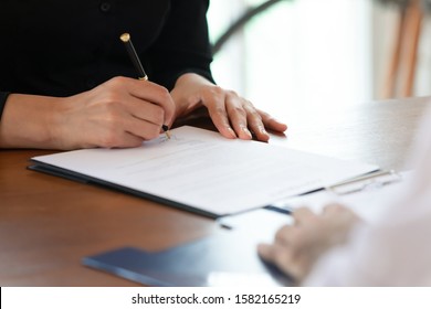 Close up cropped image young woman signing business agreement with partner after reading terms of conditions. Millennial lady putting signature on contract or insurance at meeting with banker lawyer.