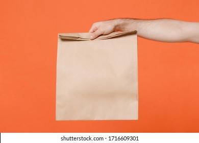 Close Up Cropped Male Hold Brown Empty Blank Paper Bag For Takeaway Isolated On Orange Background. Food Delivery Service From Restaurant Shop To Home. Epidemic Pandemic Coronavirus 2019-ncov Covid-19