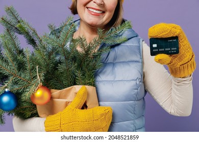 Close Up Cropped Mature Elderly Woman 55 Years Old Wears Blue Waistcoat Yellow Hat Mittens Hold Spruce Branches Show Credit Bank Card Isolated On Plain Pastel Light Violet Background Studio Portrait