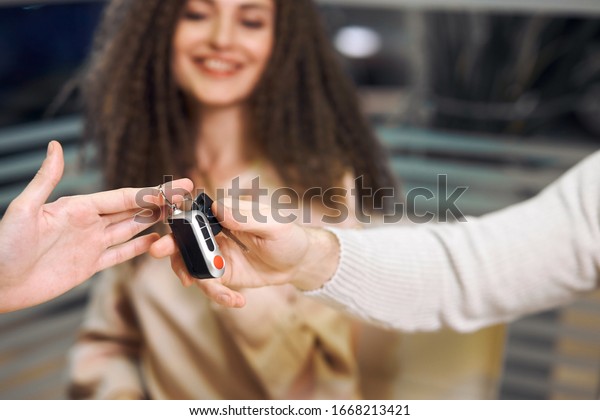 close up\
cropped photo. dealer giving car keys to a man. Copy space. smiling\
happy woman in the blurred background of the photo. bargain,\
successful shopping day,\
business