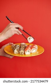 Close up cropped photo of female hand holds makizushi sushi roll served on plate traditional japanese food isolated on red background in studio. Copy space advertising mock up.