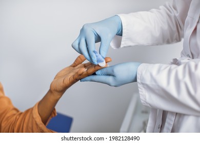 Close Up Cropped Photo Of Hands Of A Female Lab Worker In White Coat And Gloves, Taking A Patient's Blood Sample, Using Painless Scarifier. Black Woman Patient Ready To Blood Test