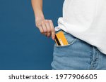 Close up cropped photo portrait shot of caucasian female hand arm putting credit bank card in jeans pants denim pocket isolated on dark blue background studio portrait. Money finance currency concept