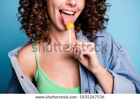 Close up cropped photo of positive cheerful girl enjoy summer time weekend, lick tongue lollipop wear green singlet isolated over blue color background