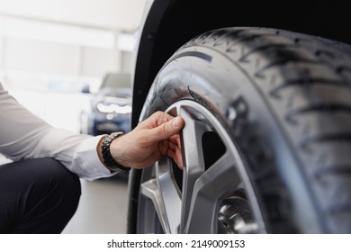 Close cropped up photo shot man hand buyer client in shirt chooses auto wants to buy new automobile touch car tire wheel disk in showroom vehicle salon dealership store motor show indoor Sales concept