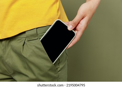 Close up cropped photo shot woman she wear yellow t-shirt holding in hand put into pants pocket mobile cell phone with blank screen workspace area card isolated on plain olive green khaki background. - Shutterstock ID 2195004795