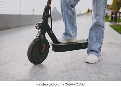 Close up cropped photo shot of young woman wear jeans denim pants casual clothes riding electrical scooter transport vehicle walk rest relax in city park outdoors on nature. Urban lifestyle concept - Powered by Shutterstock