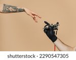 Close up cropped photo of tattooer master artist male hold in hand machine black ink in jar, equipment for making tattoo art on body, touch female finger arm isolated on pastel plain beige background