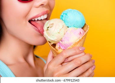 Close up cropped photo of young happy girl licking yummy ice cream of three scoops of different flavors, on yellow background, in sun glasses