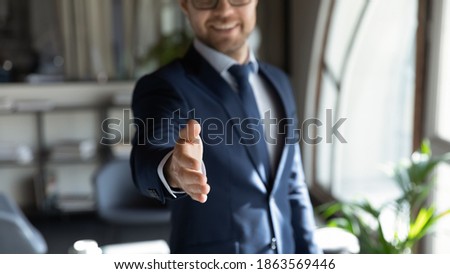 Close up cropped portrait of smiling successful friendly young man in formal attire hr recruiter stretching hand to camera glad to offer you job in company, greeting spectator as new workforce member