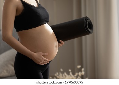 Close up cropped pregnant woman touching belly, holding yoga mat, young future mom ready for training, physical activity, gymnastics or exercises during pregnancy concept, healthy lifestyle and sport