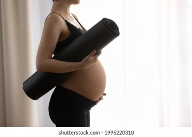 Close up cropped profile of pregnant woman in black sportswear holding yoga mat, touching belly, young future mom ready for gymnastics or exercise, healthy lifestyle and sport during pregnancy