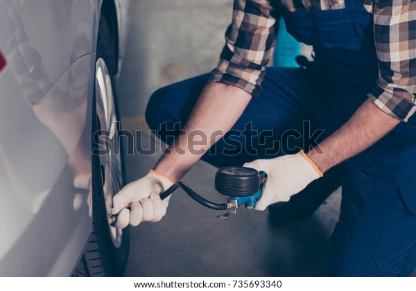 Close up cropped shot of expert`s specialist
technician hands, checking tire physical pressure of silver car on
hardware, at auto workshop, arms in white knitted gloves, wears
special uniform overall
