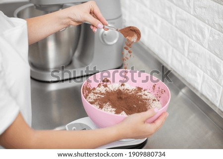 Close up cropped shot of hands of professional woman chef, pouring cacao powder into the bowl with white flour. Making macarons, cakes and desserts