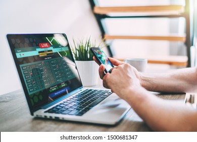 Close up cropped shot of male hands making bets using gambling mobile application on his phone. Man watching football match online broadcast on his laptop waiting for winning results. - Shutterstock ID 1500681347
