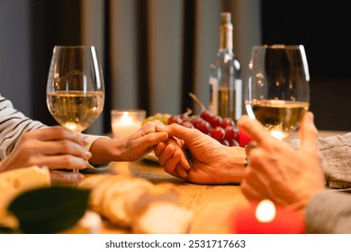 Close up cropped shot of the table during romantic dinner with lover`s hands with glasses of wine and food. Love and relationship, dating concept. Anniversary, proposal, Valentine`s Day celebration