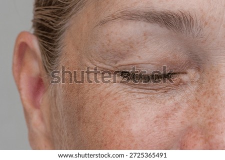 Close up cropped view of a middle aged smiling woman with wrinkles around her closed eye