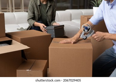 Close up cropped view, wife put things in carton box, husband use adhesive tape sealing cardboard box, young family prepare stuff for move-out. Bank loan, tenant, relocation delivery services concept - Shutterstock ID 2067029405