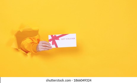Close up cropped woman hand hold gift certificate card coupon voucher on birthday holiday party or store isolated through torn yellow background studio. Copy space text place. Advertising area mock up