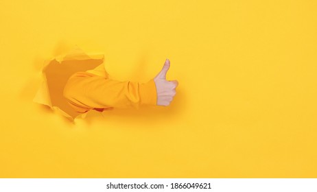 Close up cropped woman hand showing thumbs up gesture like sign isolated through torn yellow background studio. Copy space place for text image promotional content Advertising area workspace mock up