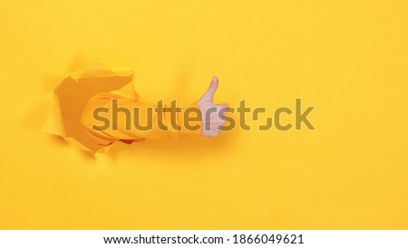 Close up cropped woman hand showing thumbs up gesture like sign isolated through torn yellow background studio. Copy space place for text image promotional content Advertising area workspace mock up