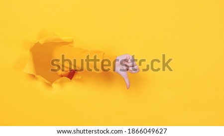 Close up cropped woman hand showing thumb down gesture like sign isolated through torn yellow background studio. Copy space place for text image promotional content Advertising area workspace mock up