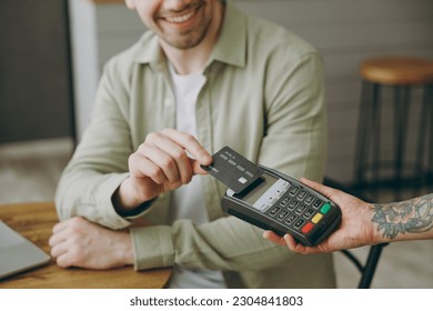 Close up cropped young man sitting alone at table in coffee shop cafe indoors work laptop pc computer hold bank payment terminal process acquire credit card Freelance mobile office business concept - Powered by Shutterstock