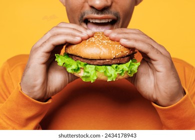 Close up cropped young man wear orange sweatshirt casual clothes holding eating biting burger isolated on plain yellow background studio. Proper nutrition healthy fast food unhealthy choice concept - Powered by Shutterstock